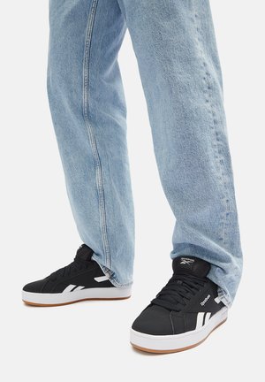 Mustad mustad spordijalatsid valgete detailidega, kummist tallad ja tekstuuriga kangas, kantud laia helesinise teksapükstega.