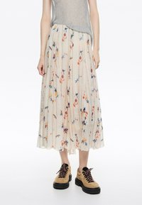 Falda midi fluida hecha de tela ligera, con un fondo crema, estampados florales coloridos y textura plisada. Combinada con botas con cordones.