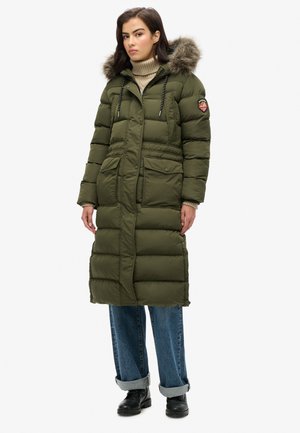 Long olive green puffer coat with fur-lined hood, two front pockets, and a zippered closure. Worn with blue wide-leg jeans and black boots.