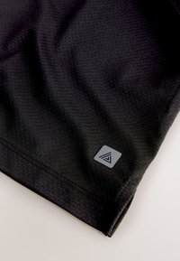 Close-up of black textured fabric with a small gray square logo near the hem on a light background.
