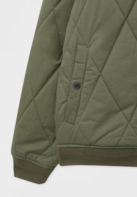 Manche et poche de veste vert olive matelassées avec bouton-pression, poignet côtelé et motif de couture en losanges.