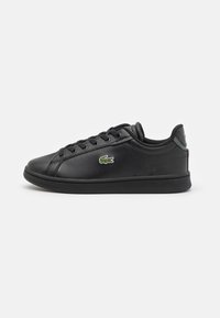 Sneaker en cuir noir avec bout rond, fermeture à lacets à l'avant et semelle en caoutchouc texturée. Présente un petit logo crocodile vert sur le côté.