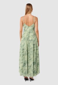 Long, flowy green dress with a marbled pattern, spaghetti straps, and a deep V-back, paired with black high-heeled shoes.