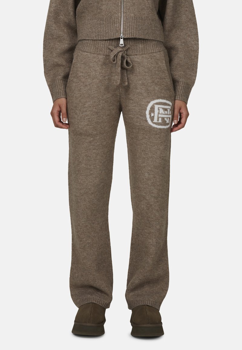 Brązowe dzianinowe spodnie dresowe z regulowanym paskiem w talii i białym logo. Posiadają ściągacze przy nogawkach oraz miękką teksturę.