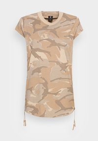 Camiseta de manga corta en camuflaje beige con cuello redondo, que presenta detalles con cordón en el dobladillo y una textura suave y lisa.