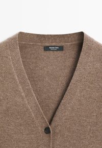 Cardigan marrone con bottoni, design a V, realizzato in tessuto texturizzato. Presenta un singolo bottone nero e un'etichetta del marchio all'interno del colletto.