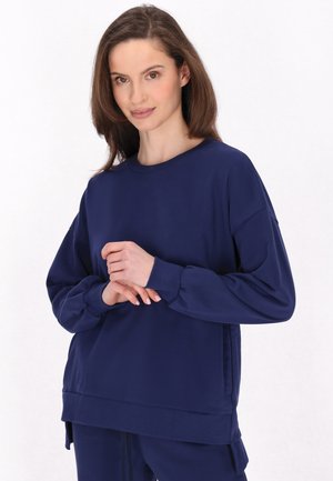 Sweatshirt bleumarin, cu mâneci lungi, croială lejeră, guler rotund, material moale, manșete ribbate, fante laterale la tiv. Textură netedă cu detalii minime.