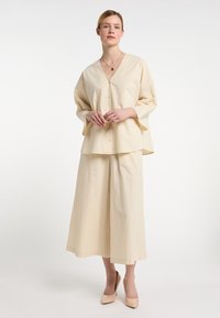 Cremfarbige, lockere Bluse mit V-Ausschnitt und Knöpfen, kombiniert mit weiten Culottes. Glatte Textur, minimalistisches Design, weiche Drapierung.