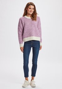Kötött pulóver lila kockás mintával, krémszínű bordás ujjak és derék. Sötétkék skinny farmernadrággal és fehér sportcipővel párosítva.