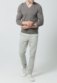 Grau V-Ausschnitt Pullover, mit gerippten Bündchen und Saum, kombiniert mit hellgrauen Slim-Fit Chinos und weißen Sneakers. Einfaches Design mit minimalen Details.