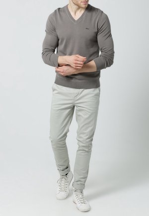 Grau V-Ausschnitt Pullover, mit gerippten Bündchen und Saum, kombiniert mit hellgrauen Slim-Fit Chinos und weißen Sneakers. Einfaches Design mit minimalen Details.