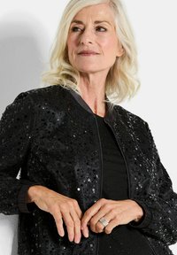 Veste bomber noire ornée de sequins noirs, avec une fermeture éclair à l'avant et des poignets côtelés. Tissu doux avec des accents brillants partout.