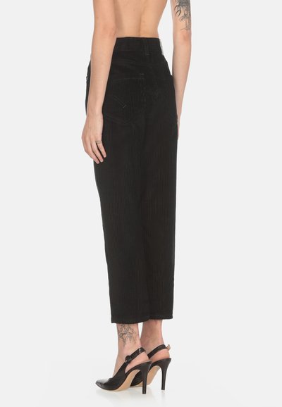 Pantaloni neri in corduroy a vita alta con vestibilità morbida e righe verticali. Presentano tasche laterali e gambe a taglio dritto. Indossati con tacchi neri.