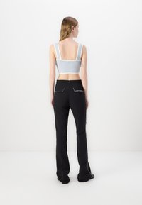 Haut court gris clair avec des bretelles larges et une texture en mesh, associé à un pantalon noir ajusté avec des coutures blanches.