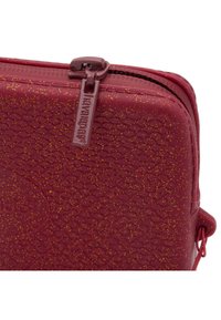 Borsa rossa con texture e finitura glitterata, dotata di chiusura con zip e tirazip con logo. Presenta angoli arrotondati e un piccolo anello laterale.