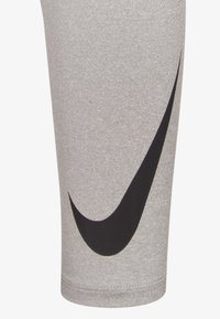 Γκρι αθλητικό κολάν κατασκευασμένο από ελαστικό υλικό, με εμφανές μαύρο λογότυπο Nike Swoosh στο εξωτερικό μέρος του μηρού. Λεια υφή.