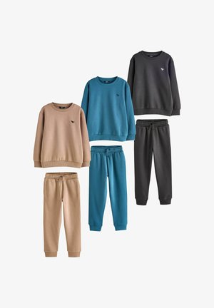 Tri kompleta dječjih dukserica i odgovarajućih trenerica u bež, plavoj i tamnosivoj boji, svaki sa malim logom dinosaura na prsima.