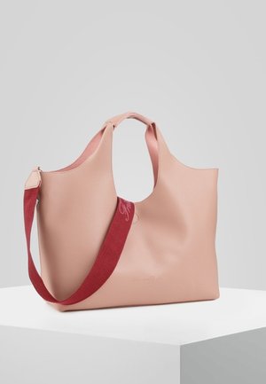 Pehmeän vaaleanpunainen nahkainen olkalaukku, jossa on kaarevat kahvat ja irrotettava leveä punainen olkahihna, esillä valkoisella jalustalla harmaata taustaa vasten.