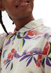 Koszula z krótkim rękawem, zapinana na guziki, wykonana z lekkiej bawełny. Posiada kolorowy wzór kwiatowy w odcieniach czerwieni, fioletu, żółci i zieleni. Z rozkładanym kołnierzykiem.