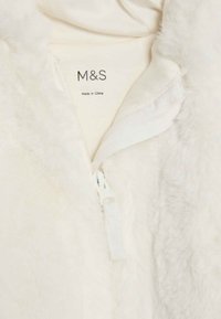Vit fluffig jacka med en delvis öppen dragkedja som visar en krämfärgad etikett invändigt märkt M&S och Tillverkad i Kina.