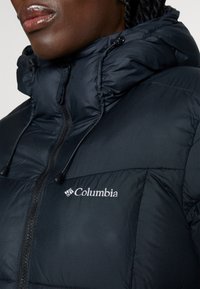 Černá péřová bunda vyrobená z syntetického materiálu, s vysokým límcem, zipem vpředu a logem Columbia na levé hrudi.