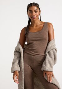 Canotta marrone a costine abbinata a leggings coordinati, completata da un leggero cardigan beige soffice con maniche ampie. Texture morbide presentate.