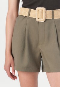 Olive spalvos šortai su klostėmis, puošti plačiu, austu smėlio spalvos diržu su kvadratiniu segtuku, dekoruotu perlų. Lygus audinys, iki kelių ilgio.