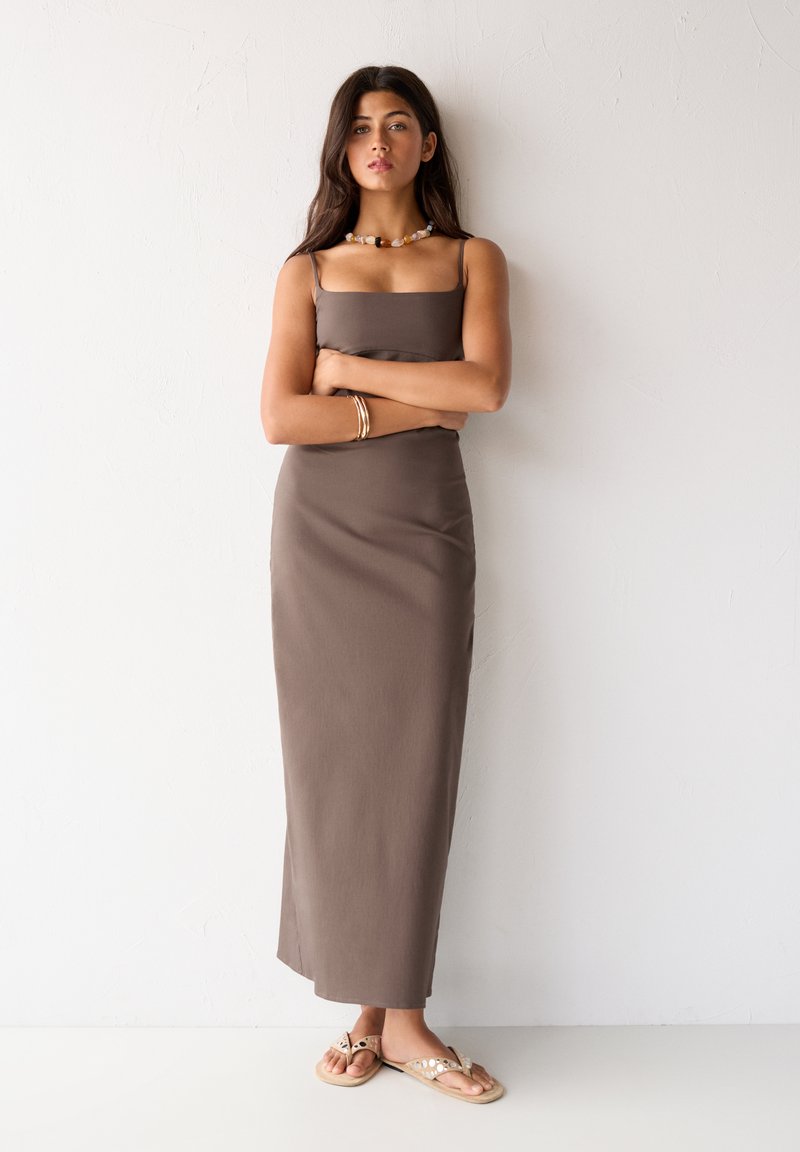Braunes, ärmelloses Maxikleid mit quadratischem Ausschnitt und glatter Textur. Getragen mit Sandalen mit floralem Muster und einer geflochtenen Halskette.