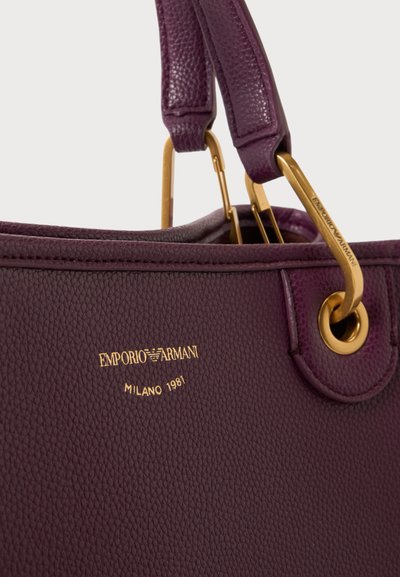 Sac à main en cuir texturé violet avec des poignées en métal doré et le logo Emporio Armani estampé en or à l’avant.