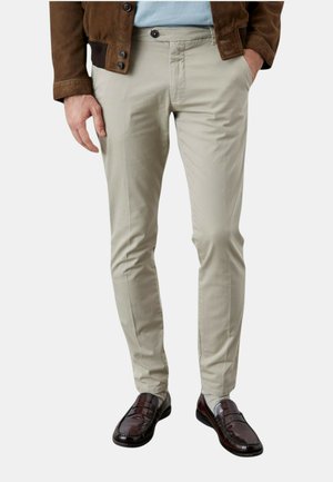 Pantaloni beige slim-fit con una superficie liscia, tasche frontali e chiusura con bottone, abbinati a mocassini marrone scuro.