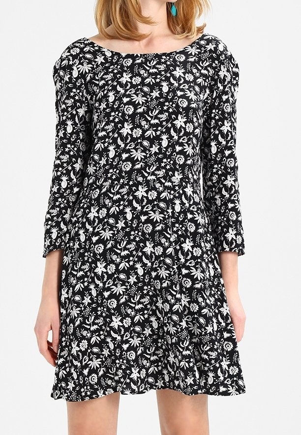 Robe noire à motifs floraux blancs, avec un décolleté bateau, des manches ballon trois-quarts et une jupe évasée. Texture en tissu doux.