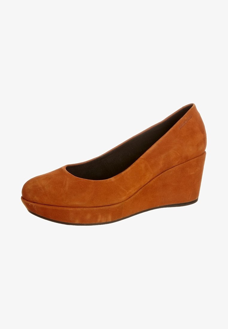 Chaussure à talon compensé en daim marron avec un bout arrondi et un avant plateforme. Le design présente une texture lisse et une silhouette élégante et épurée.
