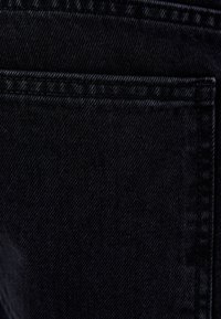 Svart denimtyg med en slät yta, som har synlig sömnad och en detalj med bakficka. Nära bild av materialet.