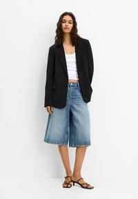 Čierny štruktúrovaný blejzer na bielom priliehavom topíku, skombinovaný so svetlomodrými denimovými culottes a hnedými sandálmi na opätku. Jednoduchý a moderný dizajn.