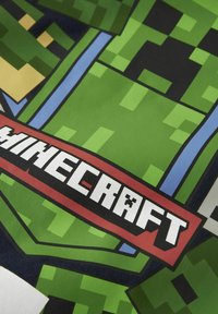 Textil temático de Minecraft en verde con diseño de personajes pixelados, con una etiqueta roja prominente que muestra "Minecraft" en texto blanco en negrita.