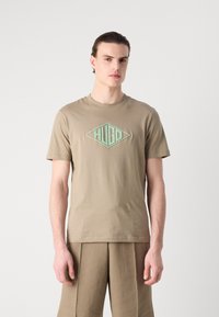 Beige bomull t-skjorte med et diamantformet logo i lys grønn. Korte ermer, rund hals, avslappet passform. Glatt tekstur, minimalistisk design.