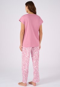 Camiseta de algodón rosa con mangas cortas combinada con pantalones rosa claro que presentan un patrón de rayas de cebra blancas. Corte relajado y diseño casual.