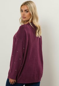 Pitkähihaista neulepuseroa syvässä purppurassa, jossa on rento istuvuus, pehmeä tekstuuri ja koristeelliset hopeiset niitit hihoissa.