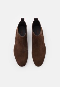 Bottes Chelsea en daim marron au design élégant, avec des empiècements élastiques sur les côtés et des languettes pour faciliter l'enfilage, forme minimaliste, texture lisse.