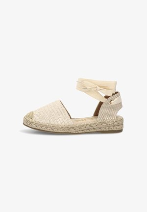 Alpargata plana beige tejida con lazo de atar alrededor del tobillo, punta cerrada y suela de yute trenzado, diseñada para un uso casual en verano.