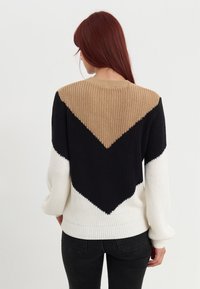 Sweter dzianinowy z wzorem w jodełkę; w kolorach czarnym, beżowym i białym. Ściśnięte ściągacze na mankietach i pasie; teksturowana dzianina.