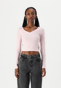 Heledad roosa ribadega pikk varrukas crop top V-kaeluse disainiga, koos kõrge vöökohaga tumedate hallide teksadega.