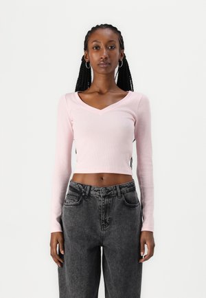 Helles rosa, geripptes Langarm-Crop-Top mit V-Ausschnitt, kombiniert mit hochgeschnittenen, dunkelgrauen Jeans aus Denim.
