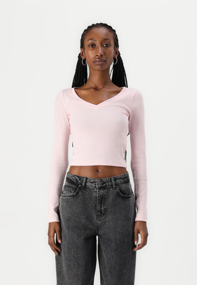 Heledad roosa ribadega pikk varrukas crop top V-kaeluse disainiga, koos kõrge vöökohaga tumedate hallide teksadega.