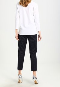 Top bianco a maniche lunghe abbinato a pantaloni neri con texture e tacchi metallici. Il top presenta un taglio dritto e un design semplice.