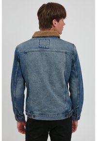 Denim jacket in light blue with a tan sherpa collar, featuring buttoned cuffs, two back pockets, and a classic straight-cut design.