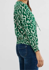 Blusa con stampa leopardo verde e bianco, con orlo e polsini elastici, abbinata a jeans in denim scuro. Tessuto dalla texture liscia e vestibilità rilassata.