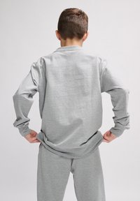 Maglietta grigia a maniche lunghe e pantaloni coordinati realizzati in tessuto morbido. La maglietta presenta un collo rotondo e una vestibilità comoda, con le maniche arrotolate.