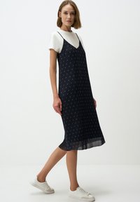 Marineblauwe slipdress met dunne bandjes en een geplooide textuur, versierd met een patroon van kleine sterren. Gecombineerd met een wit T-shirt en witte sneakers.