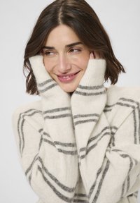 Krém színű pulóver, puha, texturált anyagból, szürke csíkokkal. Hosszú ujjakkal és laza szabással rendelkezik.